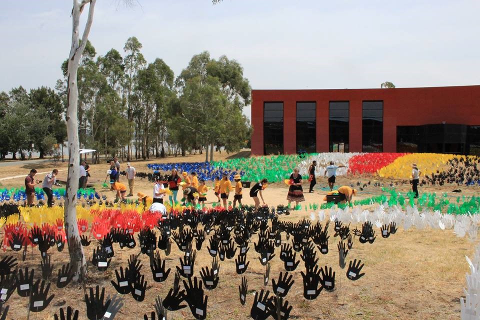 In front of the AIATSIS building, coloured hands on the mounds, school students and others planting more.