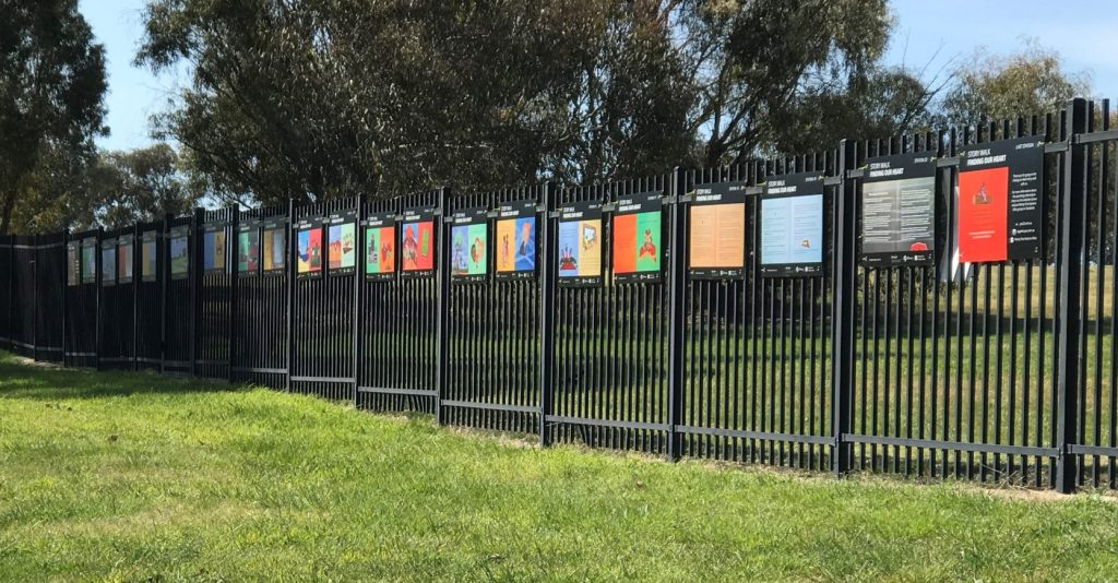 Colourful boards on fence outdoors, trees behind